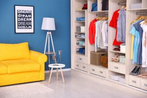Reach-in closet with custom organization system inside sitting room with bright yellow couch